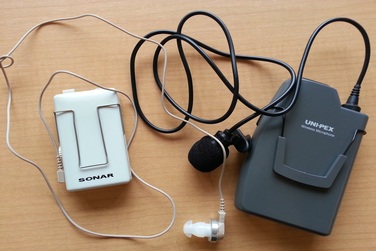 写真：左に補聴器をお持ちでない方のためのヒアリングループ受信機と、右にタイピン型ワイヤレスマイクがあります。